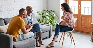 A couple sits on a couch engaged in a therapy session with a counselor, discussing and sharing their thoughts.