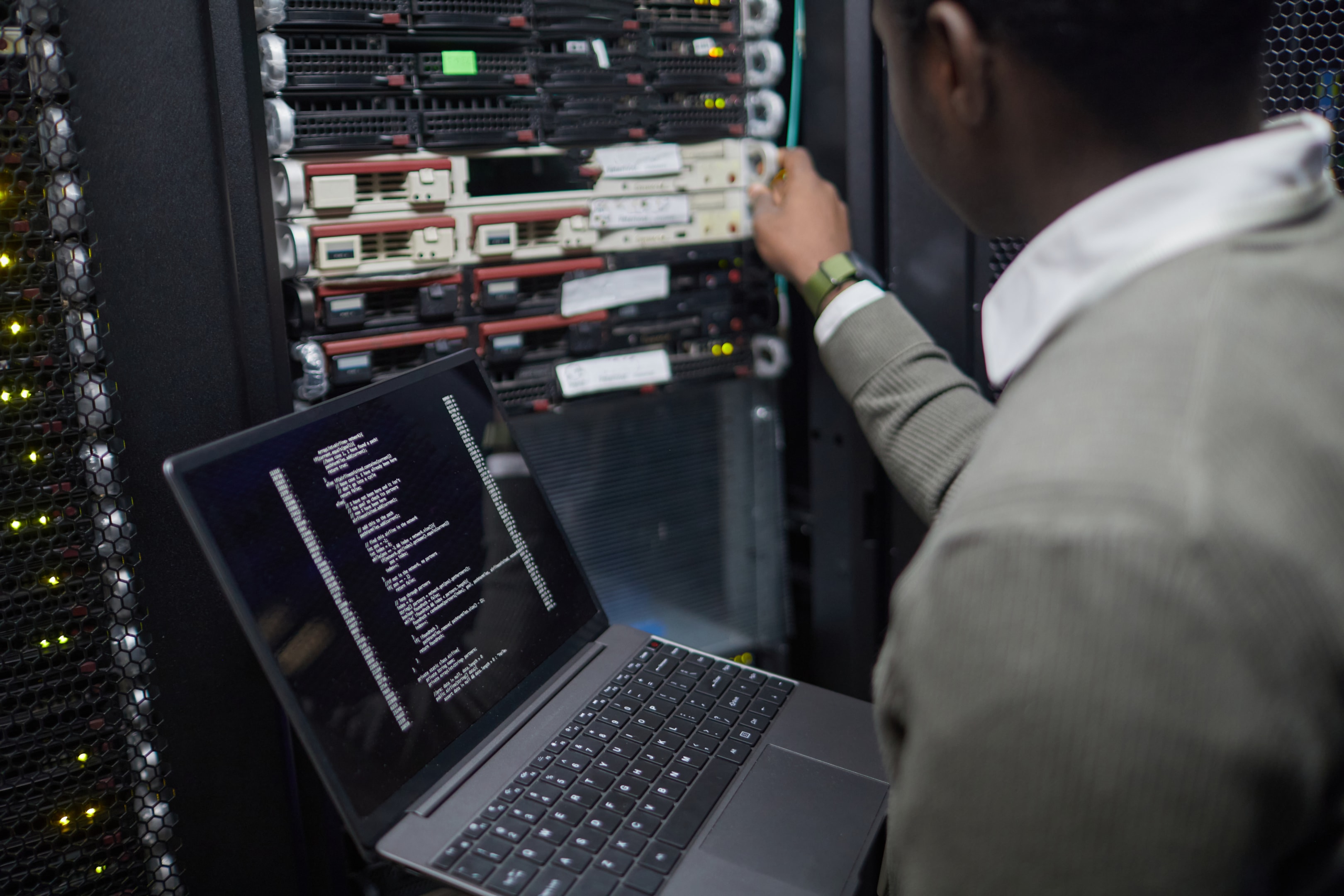 Technician working in a server room with a laptop displaying code, plugging a cable into a server rack—demonstrating hands-on support from a managed IT service provider delivering proactive IT management.