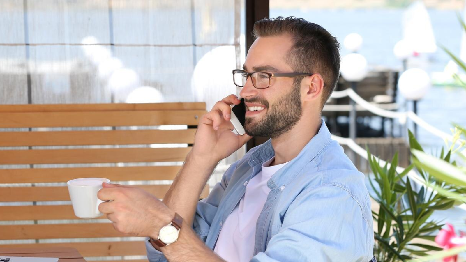 Man smiling during a phone call at an outdoor café, highlighting the ease of business calls with Simplicity VoIP & without physical hardware.