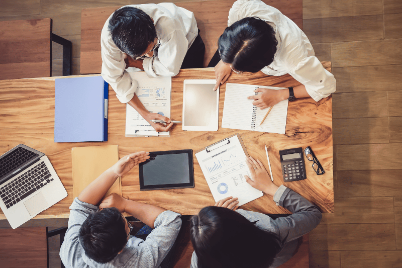 Overhead view of a startup team collaborating at a wooden table with laptops, tablets, and documents