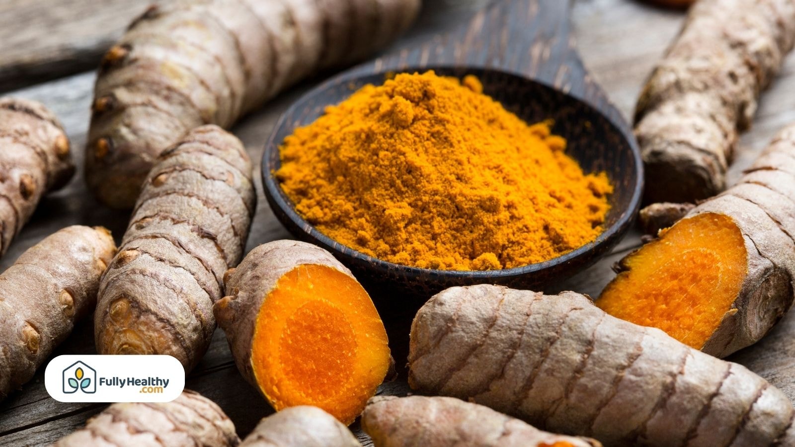 Turmeric powder in spoon surrounded by sliced turmeric roots on table