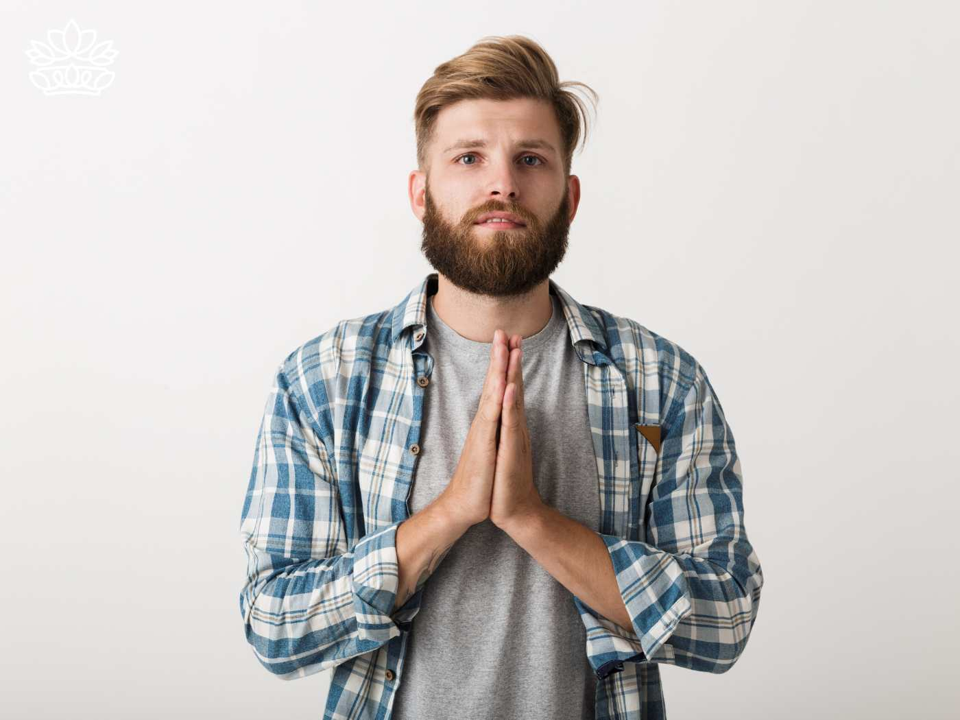 A sincere young man with a beard in a plaid shirt, pressing his hands together in a gesture of apology, expressing regret and a desire to speak and resolve hurt. This image is part of the 'I'm Sorry' Collection from Fabulous Flowers and Gifts, designed to convey love and sincerity.