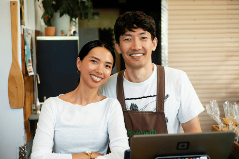 A portrait of a smiling man and woman wearing aprons behind a restaurant counter, representing small business owners who benefit from successful SEO growth.