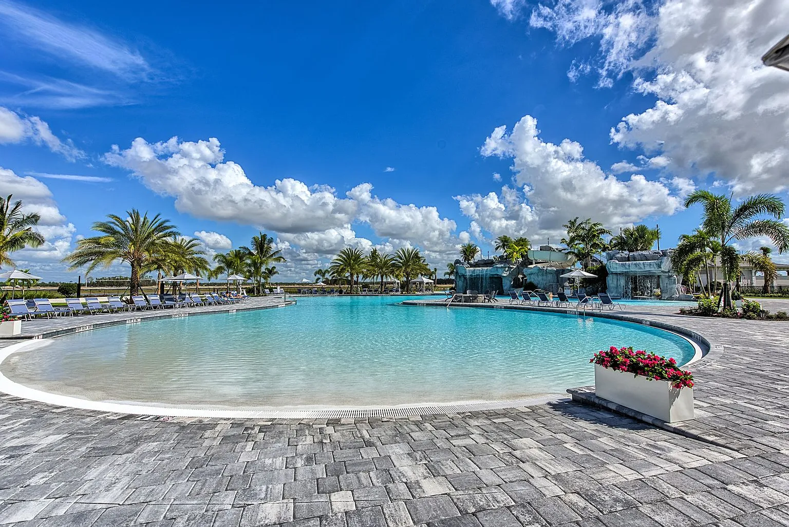The image depicts a modern single-story home featuring southern plantation styling, surrounded by lush palm trees, embodying the resort-style lifestyle typical of the Place at Corkscrew community in Estero, Florida. This property showcases a harmonious blend of elegance and comfort, reflecting the amenities and vibrant living environment available in this master-planned community.