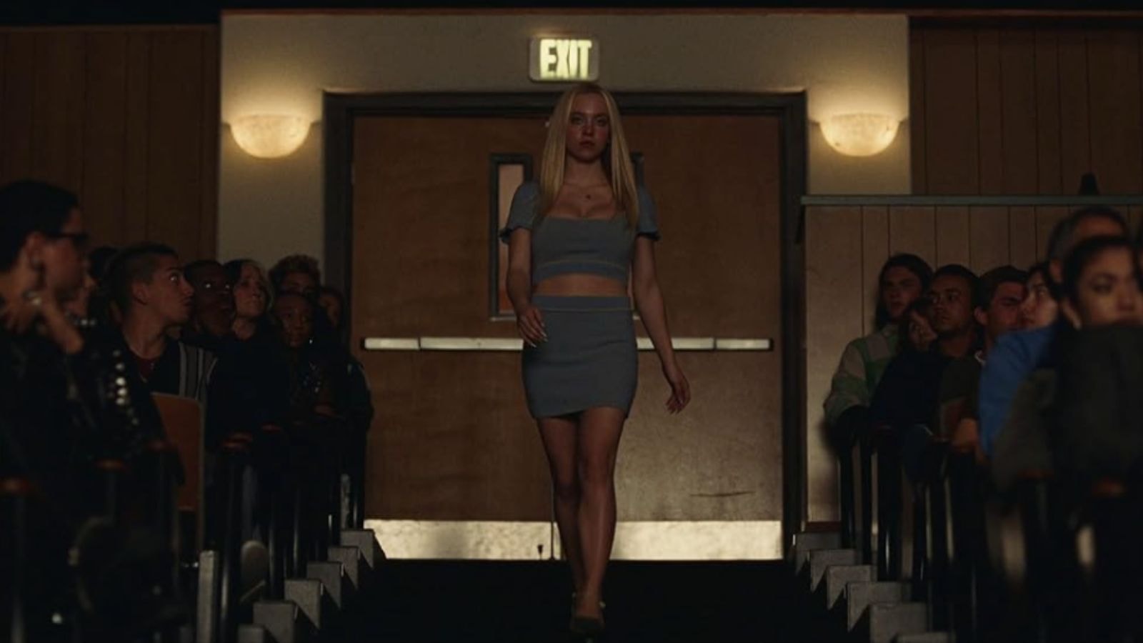Sydney Sweeney as Cassie striding down auditorium aisle under EXIT sign in Euphoria Season 2