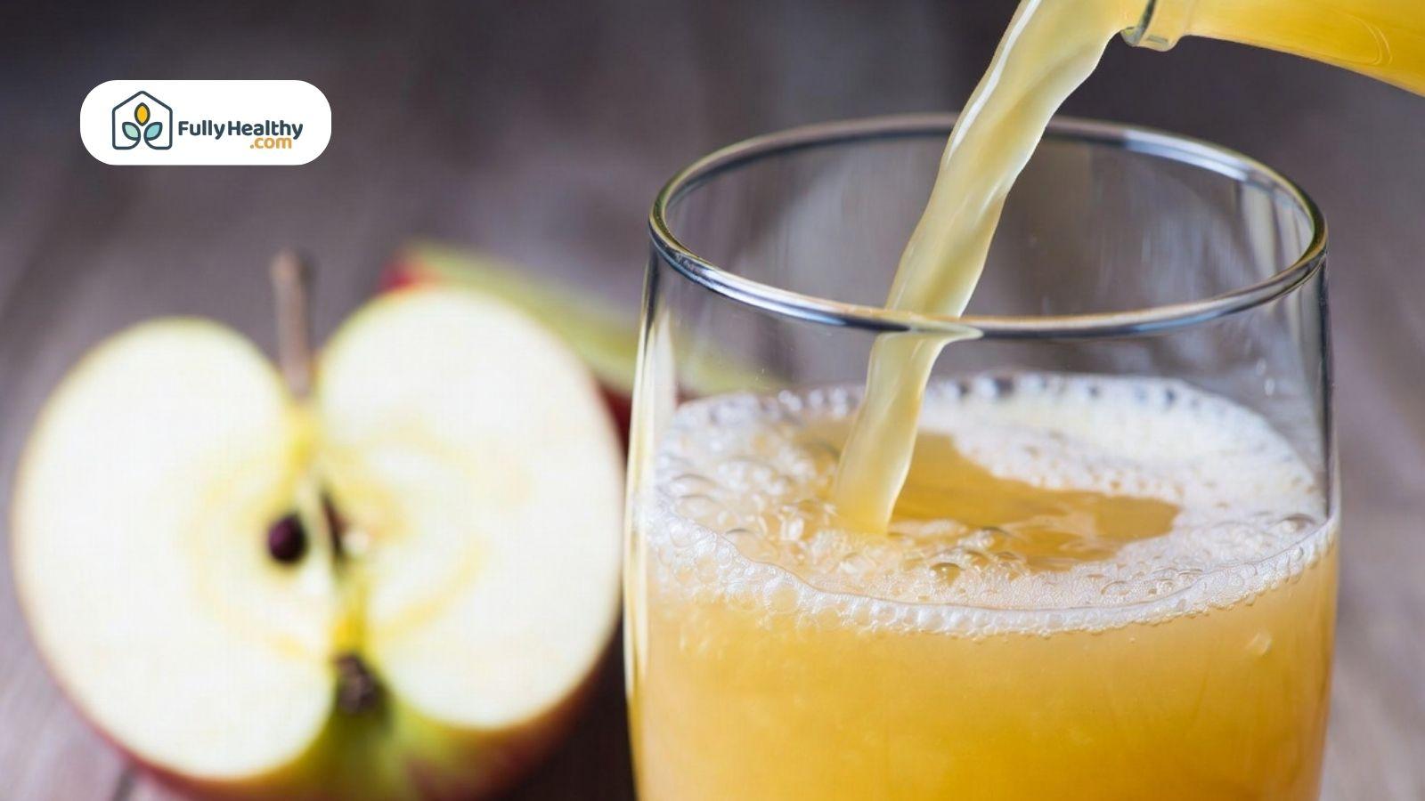 Fresh apple juice being poured into a clear glass beside sliced apples on a wooden table.