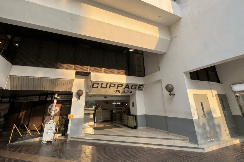 The exterior entrance of Cuppage Plaza in Singapore, showing its brutalist concrete architecture and a sign above the door reading