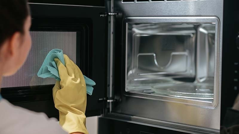 A woman wiping the inside of a microwave door