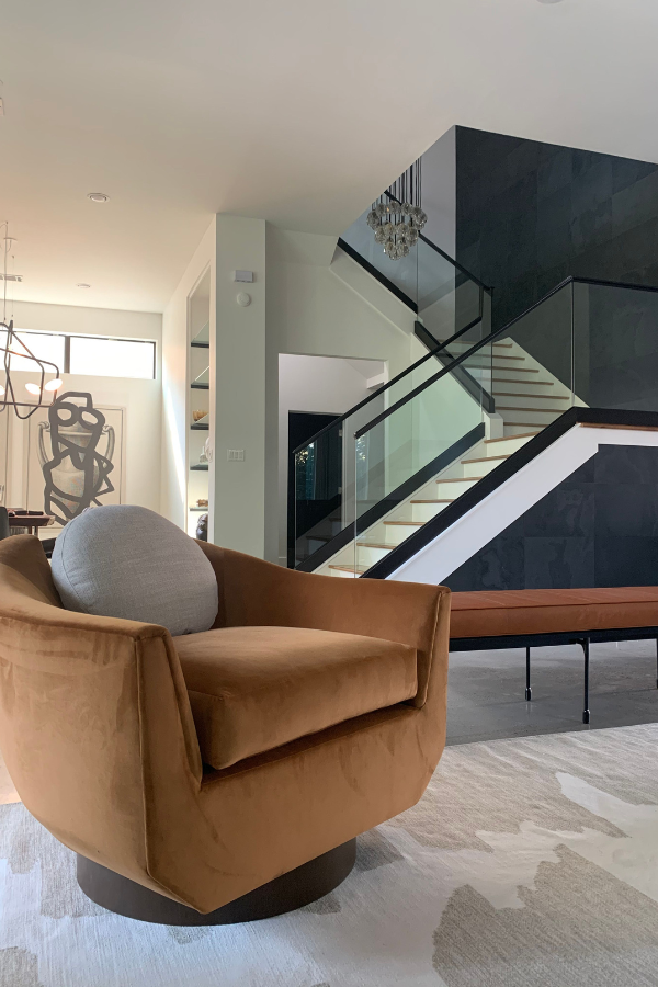 Contemporary living space with rust-colored swivel chair, glass stair railing, and abstract art in background.