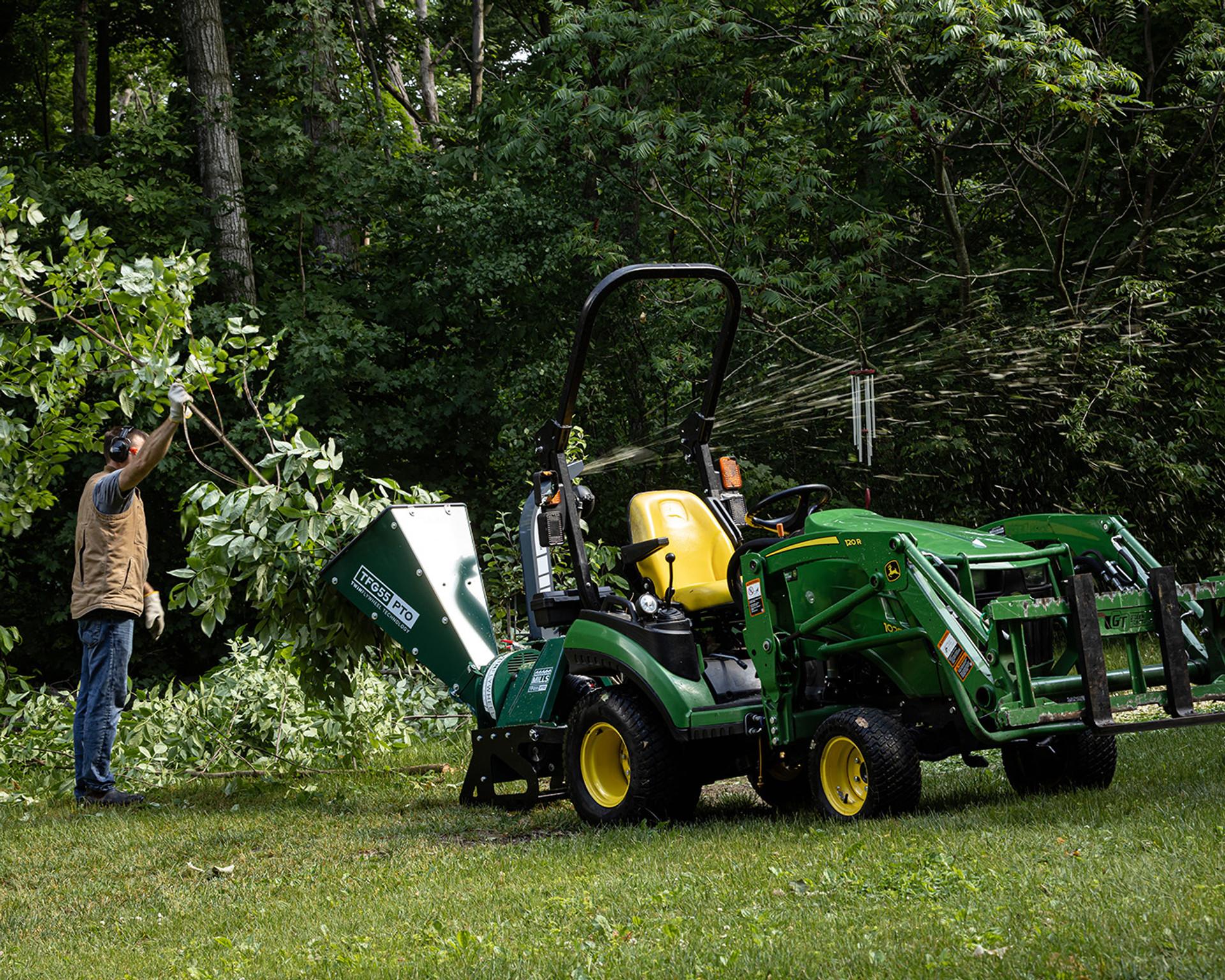 A tractor with a Woodland Mills TFG55 PTO Wood Chipper chipping trees and brush.