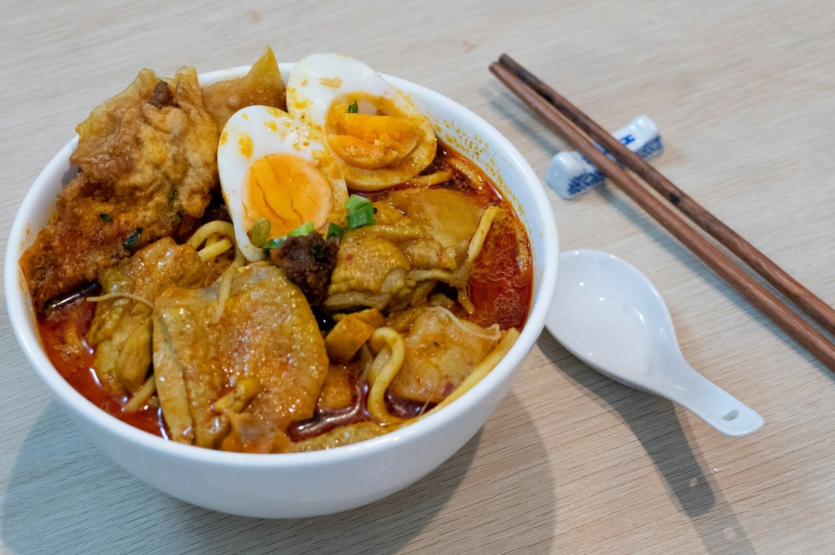 A bowl of Laksa soup with a soft-boiled egg and chopsticks, highlighting a popular dish from Chinatown.
