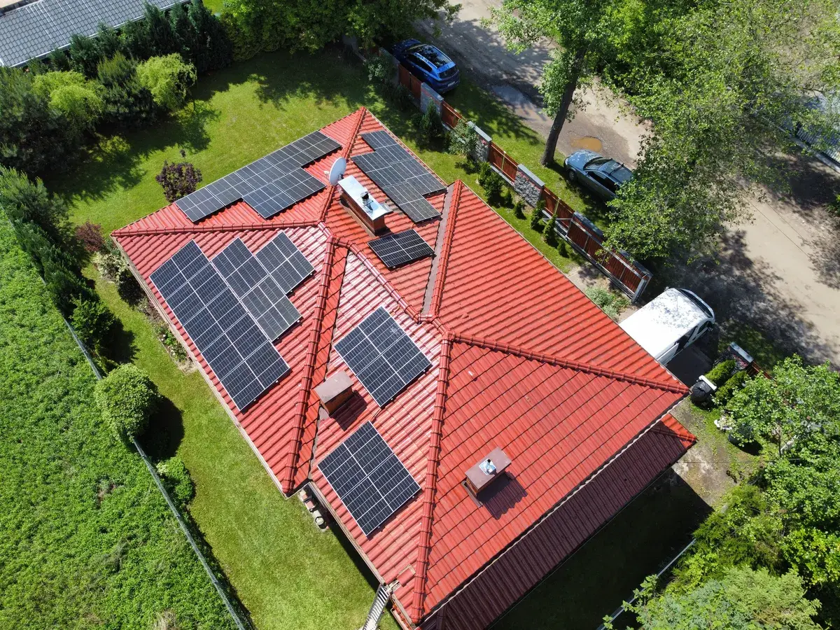 Na obrazku widać nowoczesny dom jednorodzinny z panelami fotowoltaicznymi zamontowanymi na dachu oraz magazynem energii umieszczonym przy ścianie budynku. Ta instalacja fotowoltaiczna umożliwia efektywne wykorzystanie energii słonecznej oraz jej magazynowanie, co przyczynia się do oszczędności w gospodarstwie domowym. Paneli, prąd, moc, obciążenie