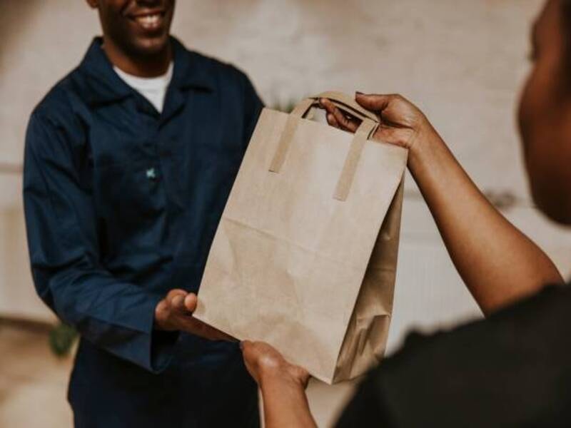 A shopkeeper handing over a brown bag to a cutomer with various items in it. The eco-friendly bag is safe for the environment and helps in carrying various items. 