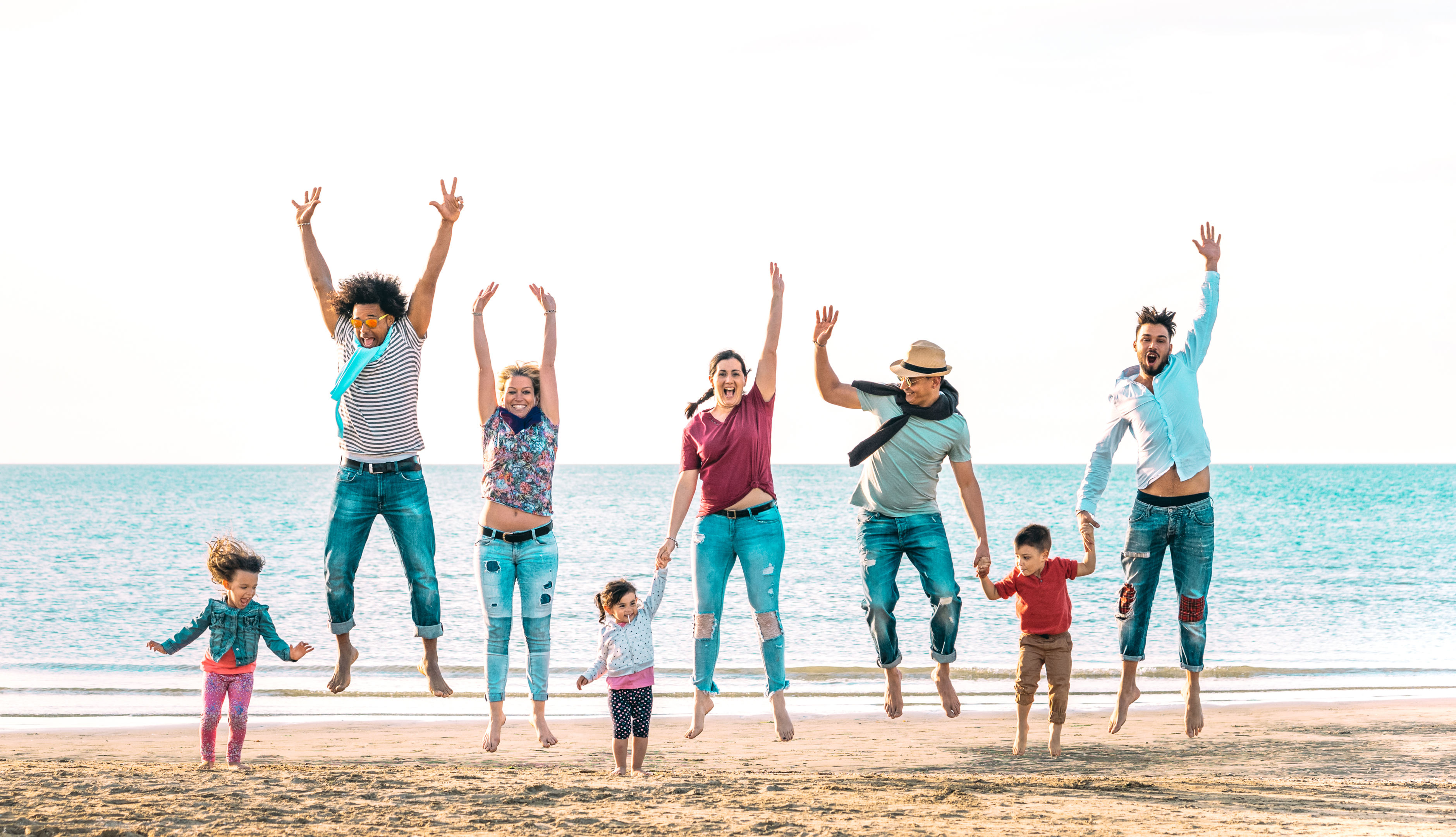 Family with small children jumping on the beach with the sea behind them