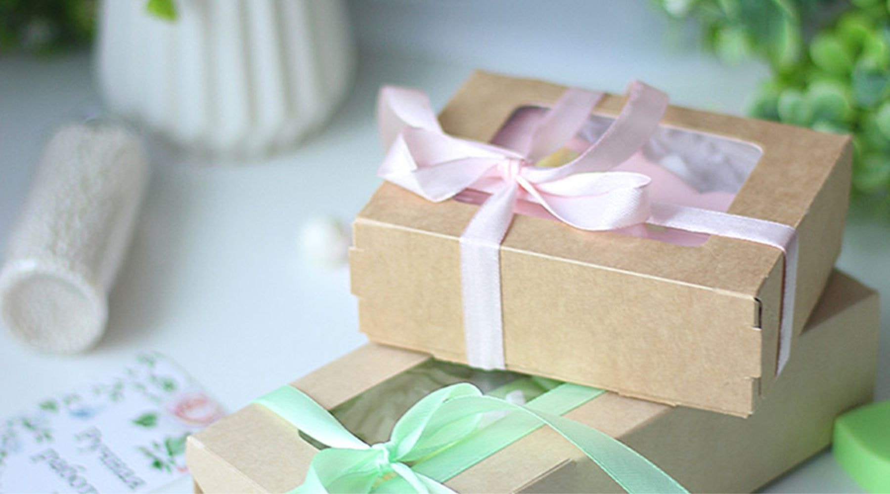 Handcrafted gift boxes tied with pastel pink and green ribbons, set on a rustic table surrounded by green plants