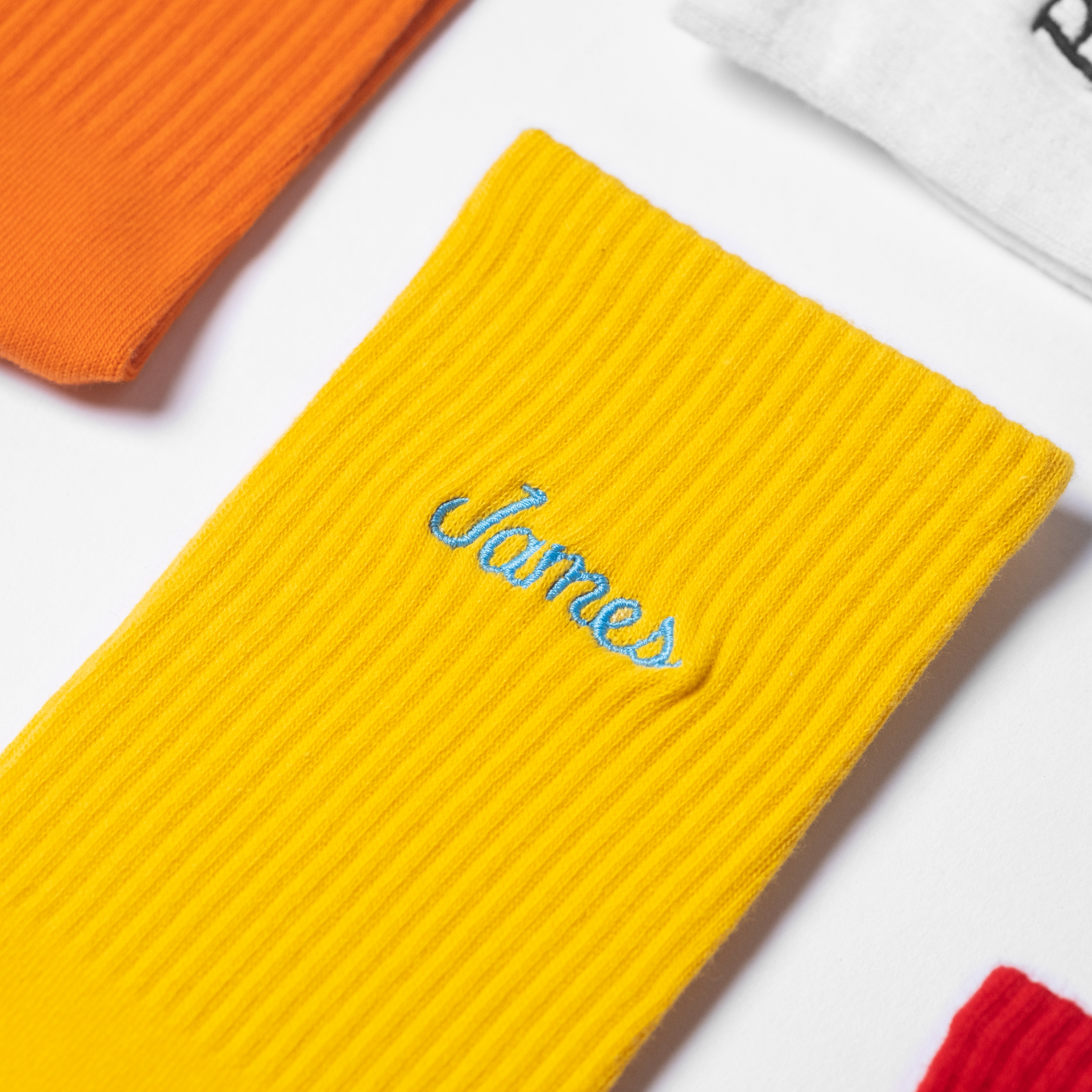 A flat-lay image of custom mens yellow crew socks with the male name 'James' embroidered in sky blue thread.