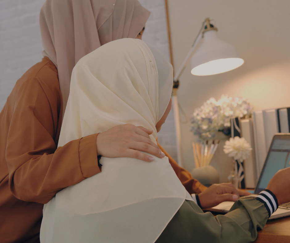 two women wearing headscarfs look at a computer