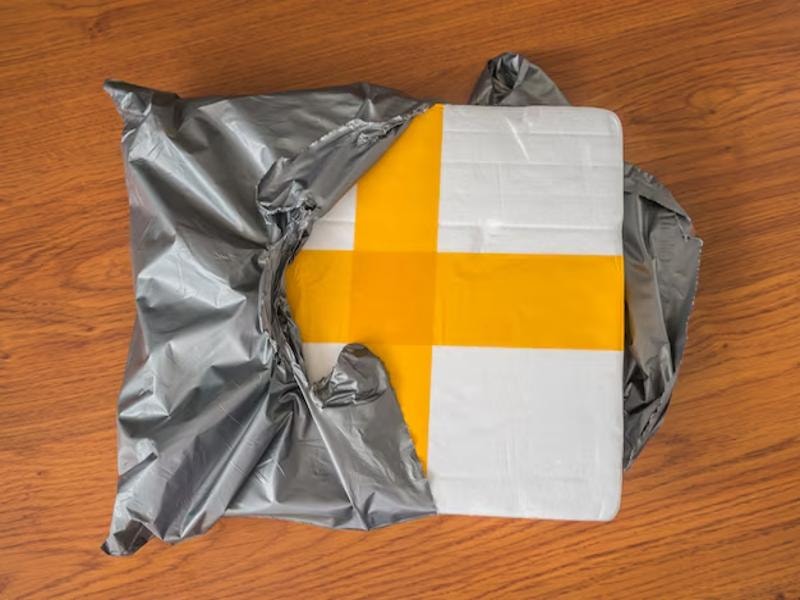 A poly mailer partially opened, revealing a Styrofoam package inside. The Styrofoam is secured with yellow tape, indicating that the contents are fragile and well-protected. The poly mailer appears to be made of lightweight, durable plastic, commonly used for shipping.