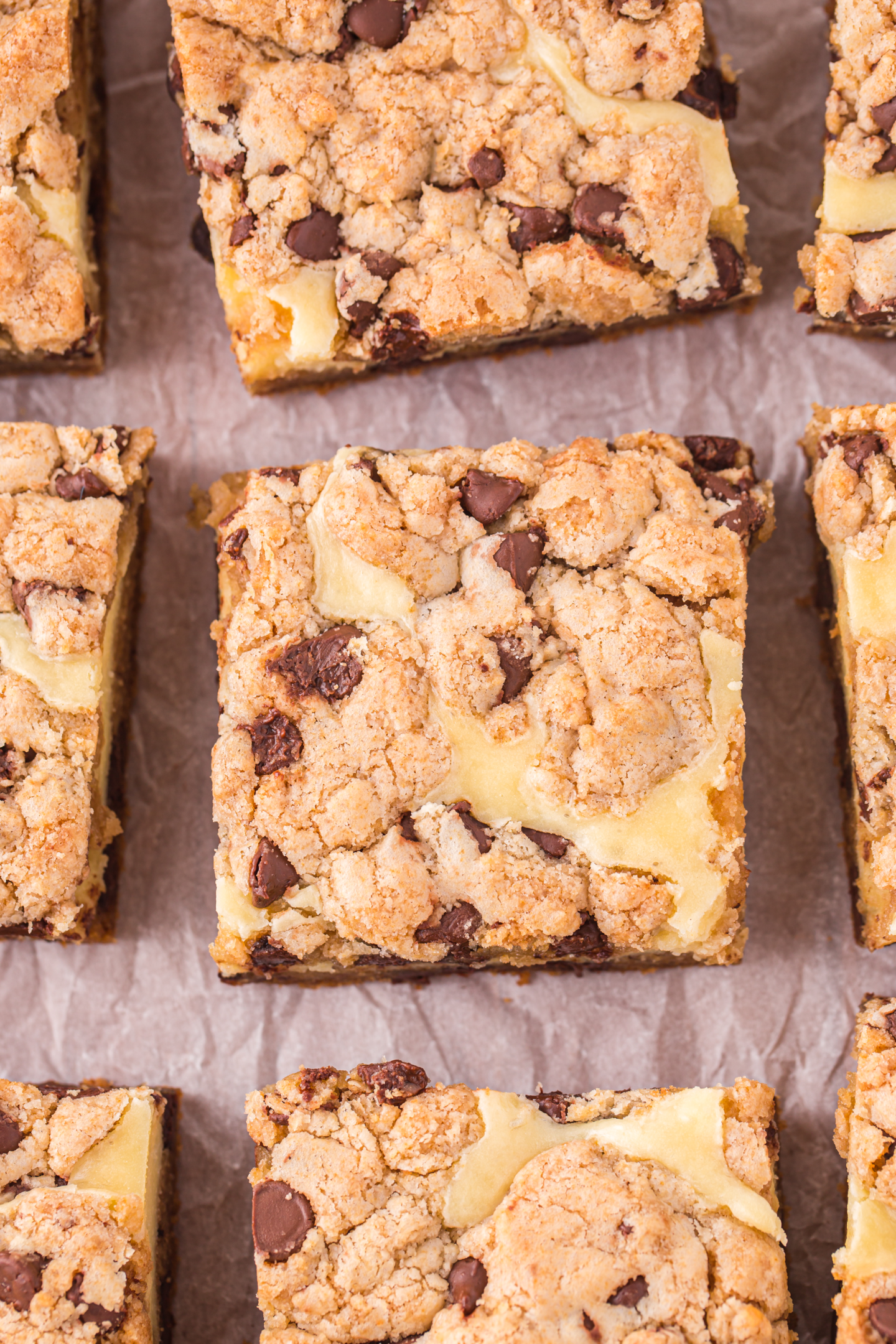 chocolate chip cookie cheesecake bars cut into squares on parchment paper