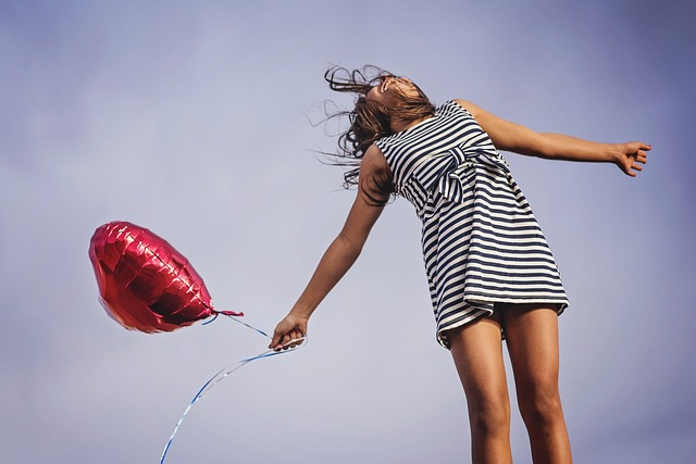 An image of a smiling woman holding a balloon and looking up at the sky in joy and freedom. 