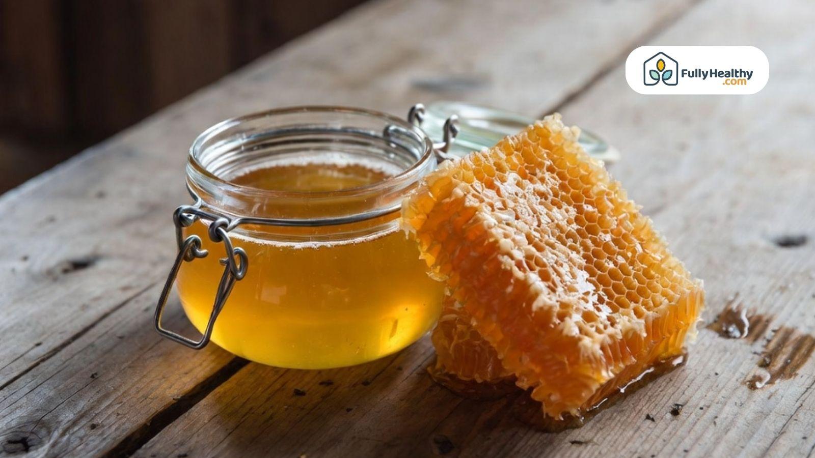 Glass jar of raw honey beside fresh honeycomb on a rustic wooden table.
