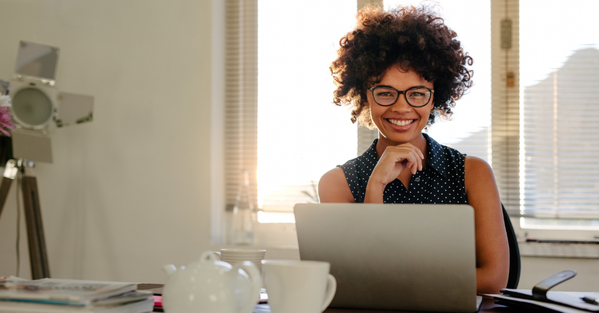 A woman smiling and looking at her laptop reading about How to file a 1099 NEC.