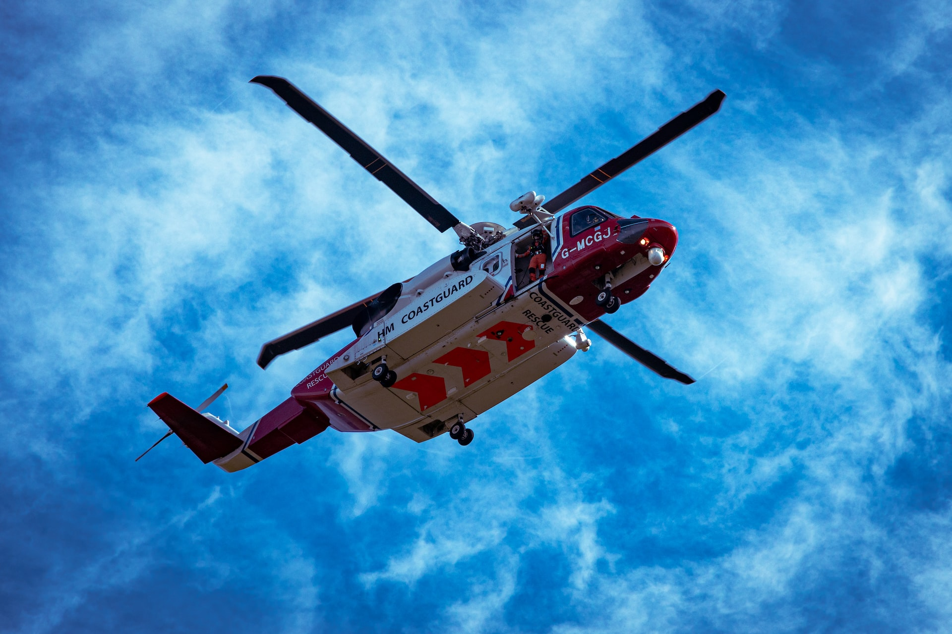 A coast guard/hospital helicopter hovering in blue sky.
