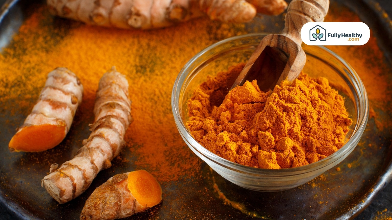 Glass bowl of turmeric powder with wooden scoop and turmeric roots
