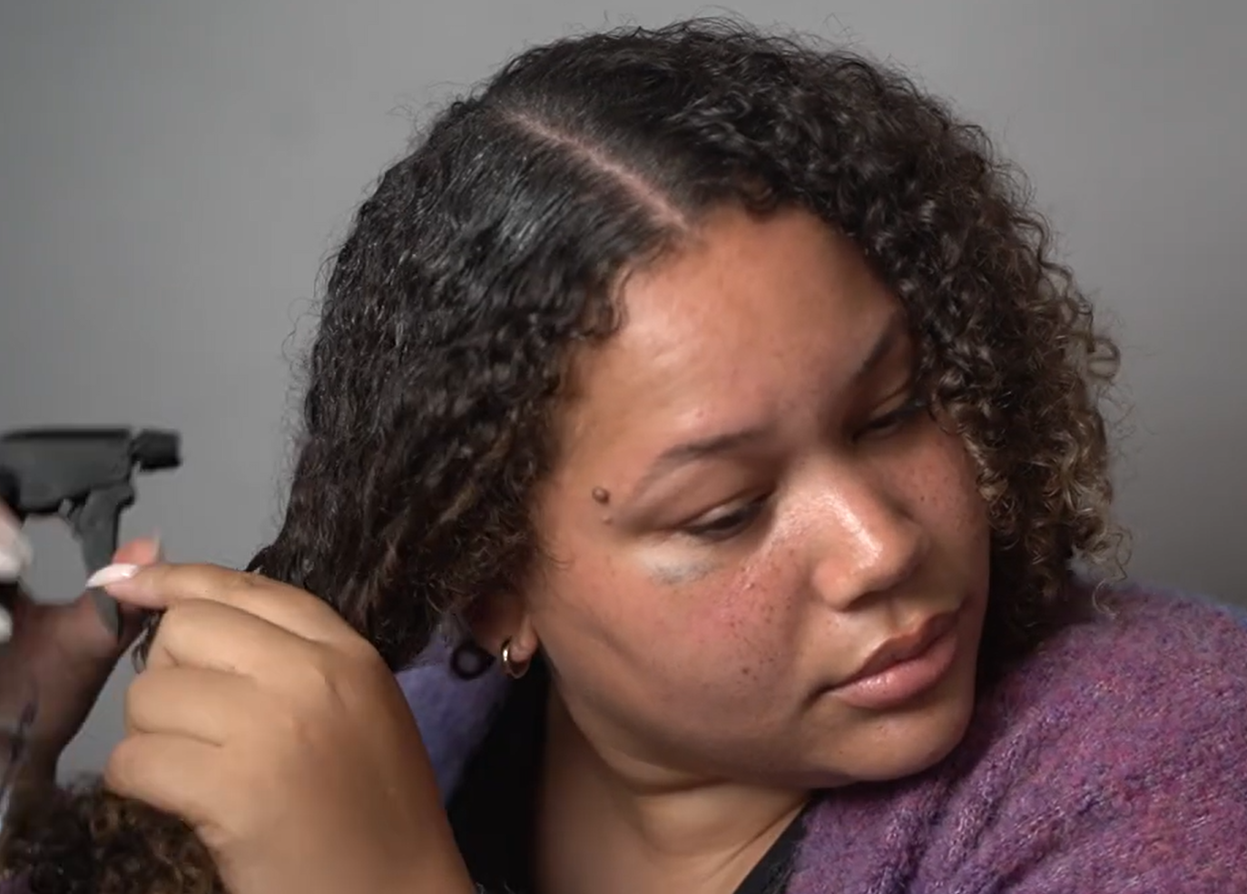 woman spraying water on her curly, frizzy hair to soften, eliminate frizz