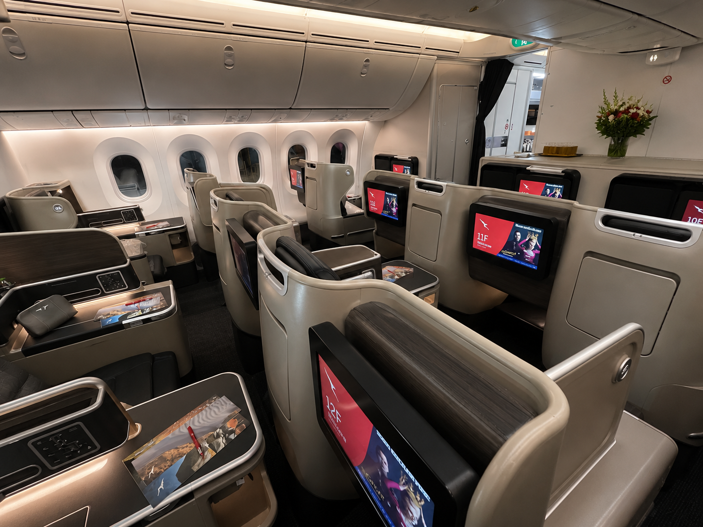 Qantas-style business class cabin with empty pod seats, entertainment screens, and wide-body aircraft windows.