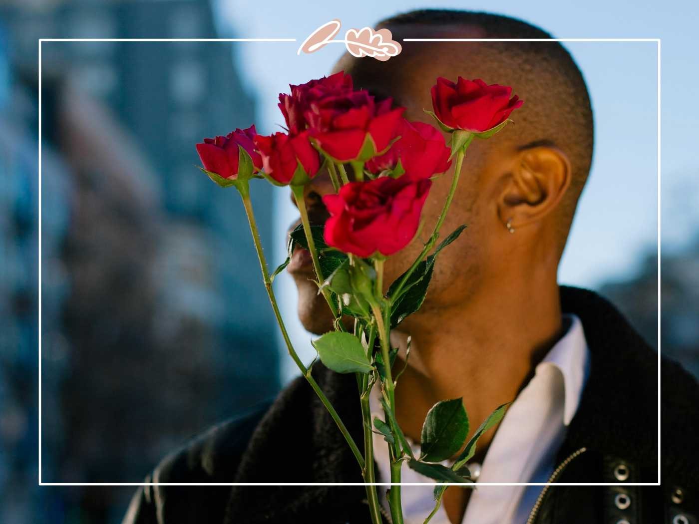 A man holding a bouquet of red roses, partially covering his face, expressing affection and mystery - Fabulous Flowers and Gifts.