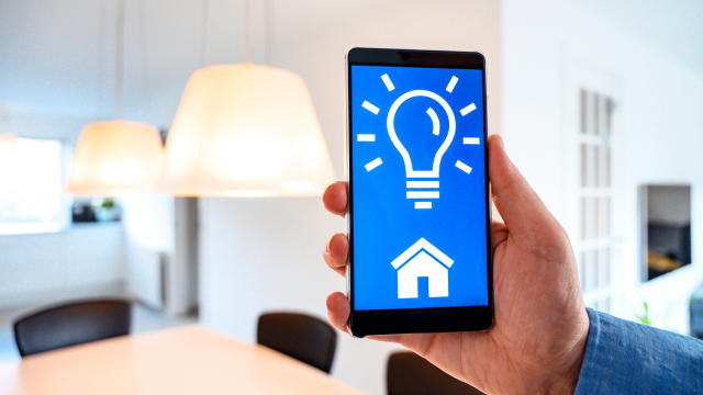 Eine Person, die ein Smartphone benutzt, um einen intelligenten Lichtschalter zu steuern, der mit einem Lichtschalter verbunden ist