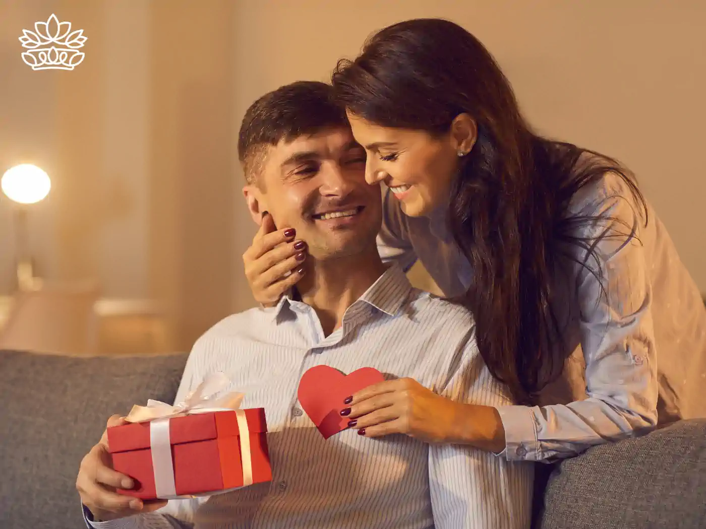 Man happily receiving a Valentine's Day gift box from a woman, expressing love and affection in a cozy home setting. Fabulous Flowers and Gifts.