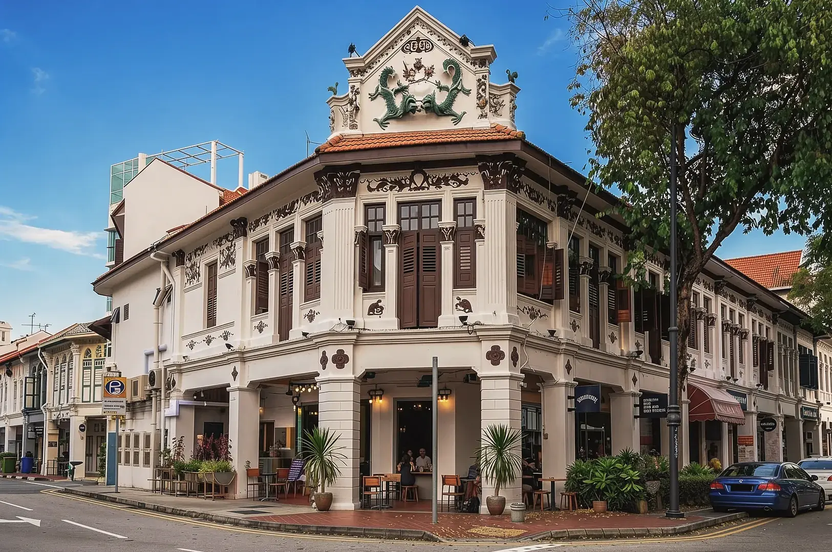 Historic corner shophouse in Singapore with ornate colonial architecture, brown shutters, and dragon reliefs, housing modern cafés and restaurants.