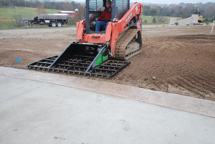 A skid steer with a landscape rake attachment leveling the ground with precision