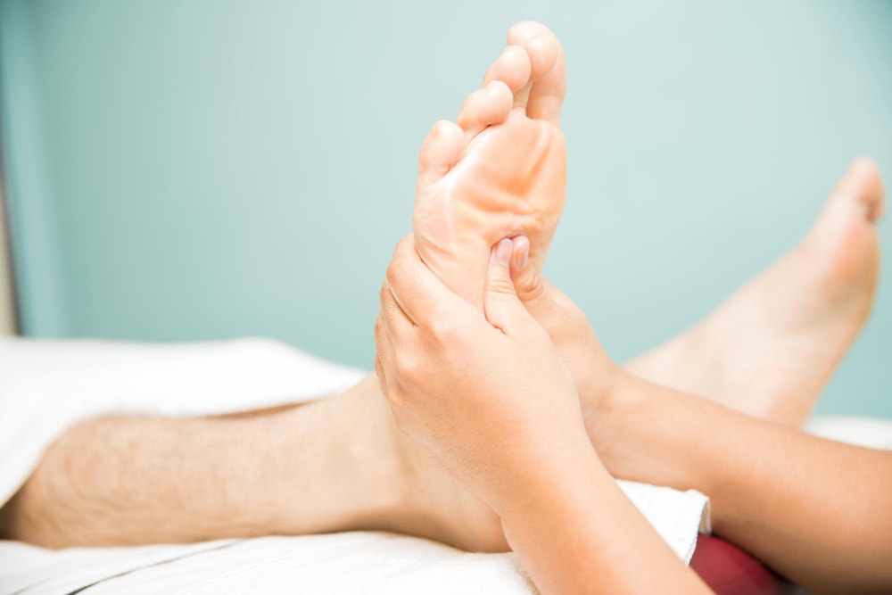 Hands pressing the arch of a patient’s foot to check for tenderness and plantar fasciitis-related heel pain.