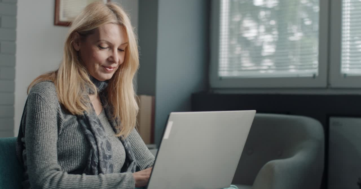 A smiling woman working on her laptop in a bright office; curious if OnlyFans tracks taxes automatically?