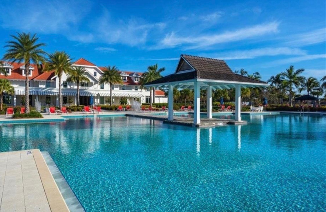 The image depicts a luxurious resort-style pool facility surrounded by tropical landscaping, featuring tennis courts and a classic clubhouse. This inviting space embodies the ultimate Florida lifestyle, making it a perfect retreat for residents of the Isles of Collier Preserve community in Naples, FL.