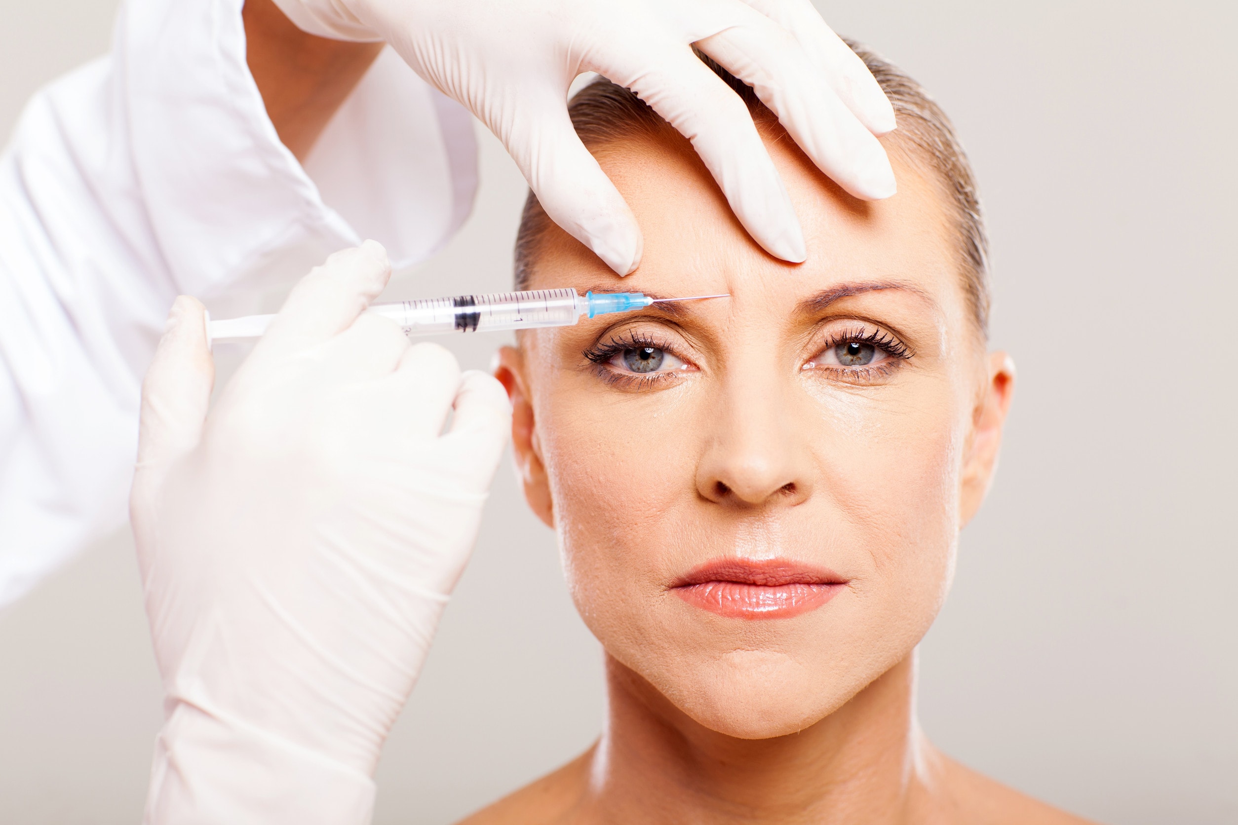 A doctor injects botox into a client's forehead.