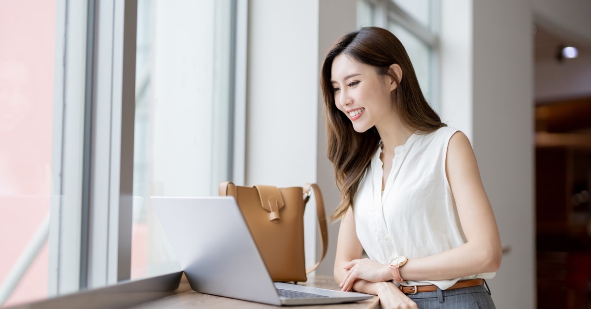 Smiling woman using a laptop by the window, finding top tax resources for OnlyFans creators.