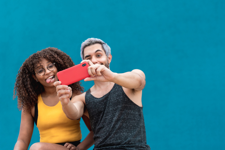 Cheerful young man and woman making funny faces and taking selfies. 