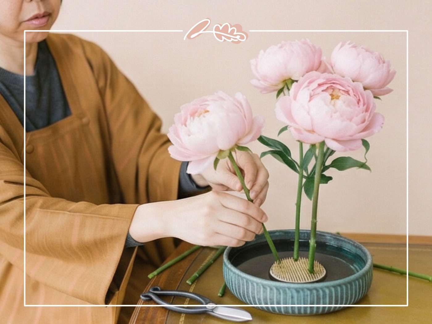 Close-up of hands carefully placing pink peony stems into a kenzan inside a teal ceramic ikebana vessel filled with water | Ikebana Technique | Fabulous Flowers & Gifts