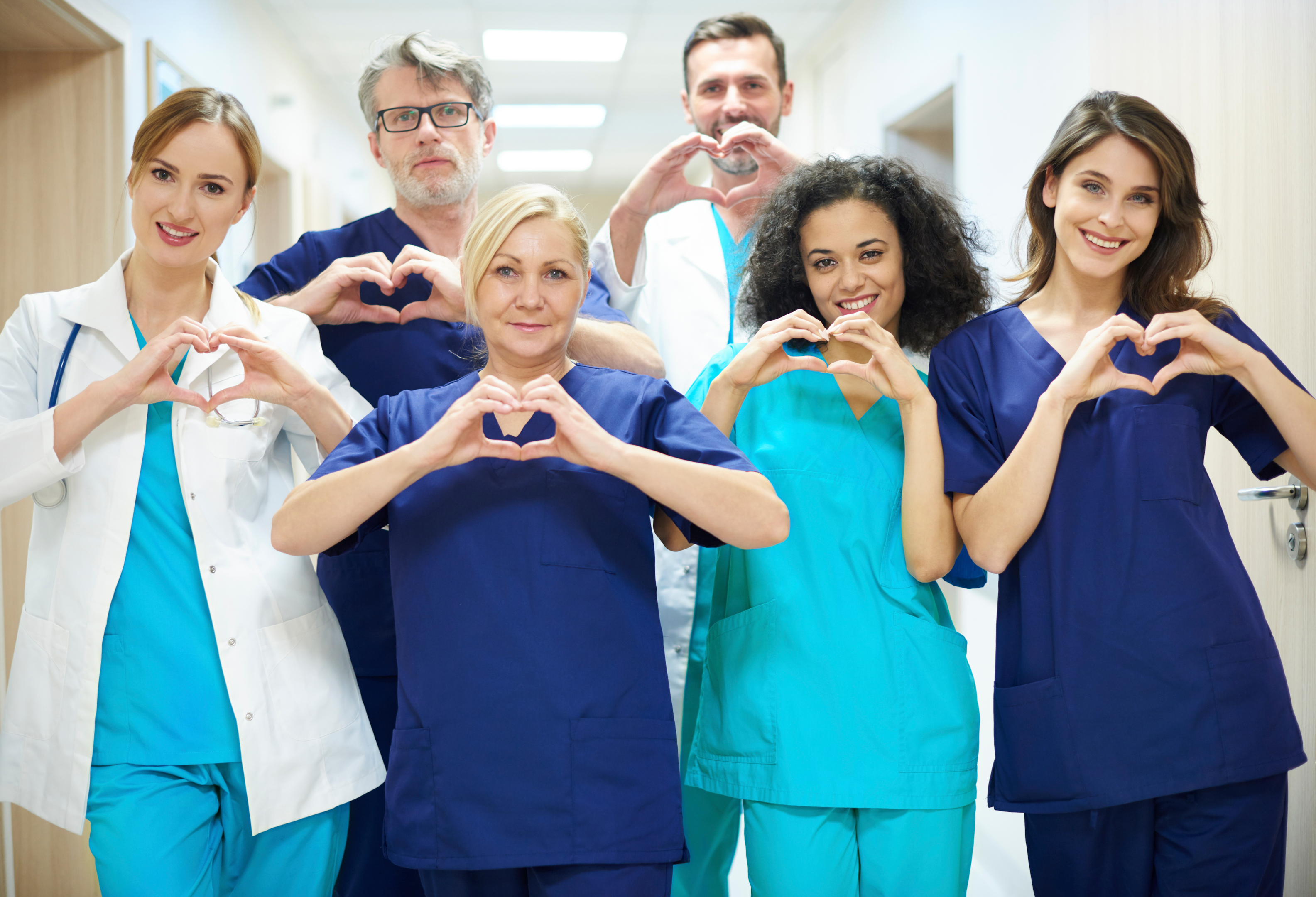 Image of several healthcare workers, in different uniforms, making heart signs with their fingers.