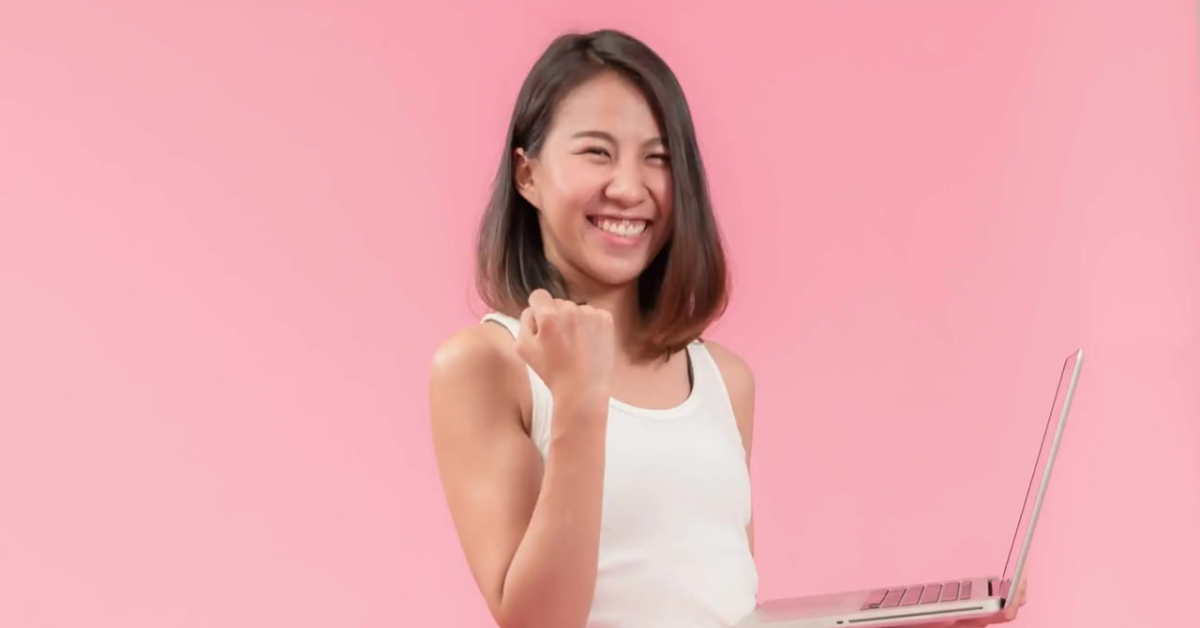 A cheerful woman holding a laptop, celebrating her understanding of what happens if you don't file taxes for OnlyFans.