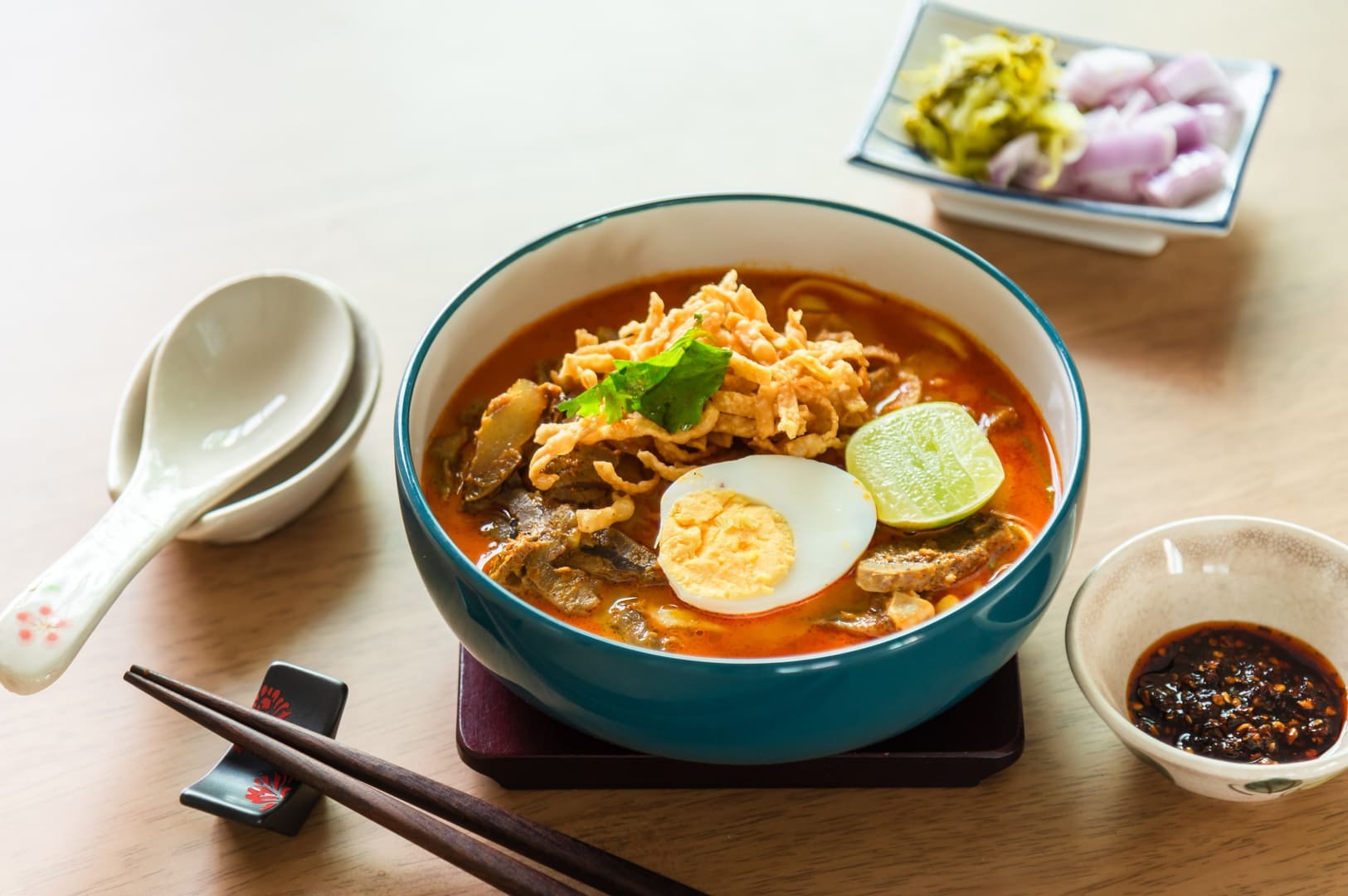 A bowl of Laksa soup topped with a soft-boiled egg and served with chopsticks.