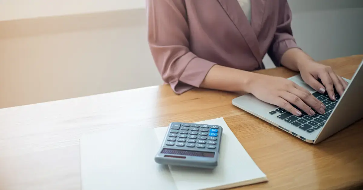 Woman reviewing budget notes with a calculator while learning what are liabilities and expenses.