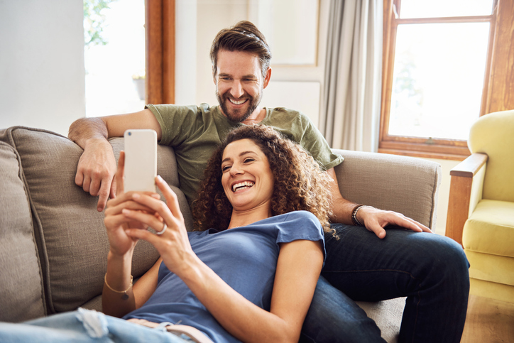 Cheerful couple relaxing on a sofa and looking at a cell phone. 