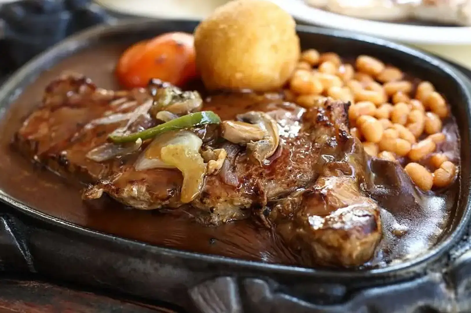 Singapore steakhouse grilled steak with mushroom sauce, baked potato and beans served on a hot plate