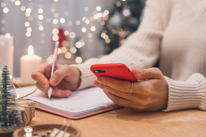 Woman making a gift list and checking her phone for deals. 