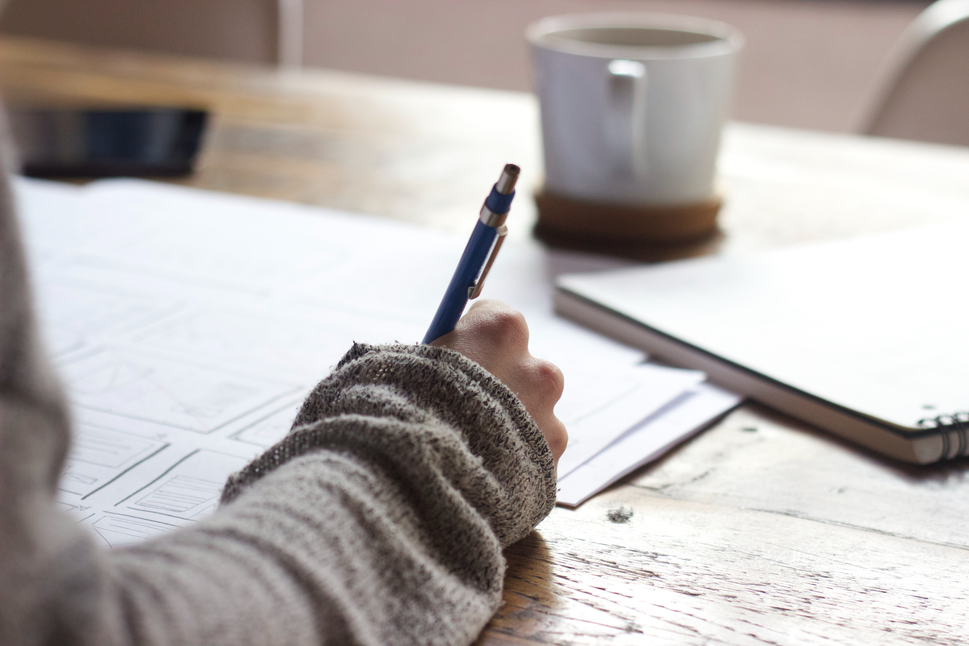 A woman at a desk, writing while enjoying a cup of coffee.